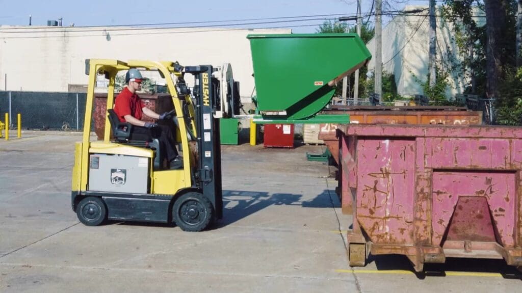 A hopper being used with a forklift. The hopper is about to be emptied into a dumpster